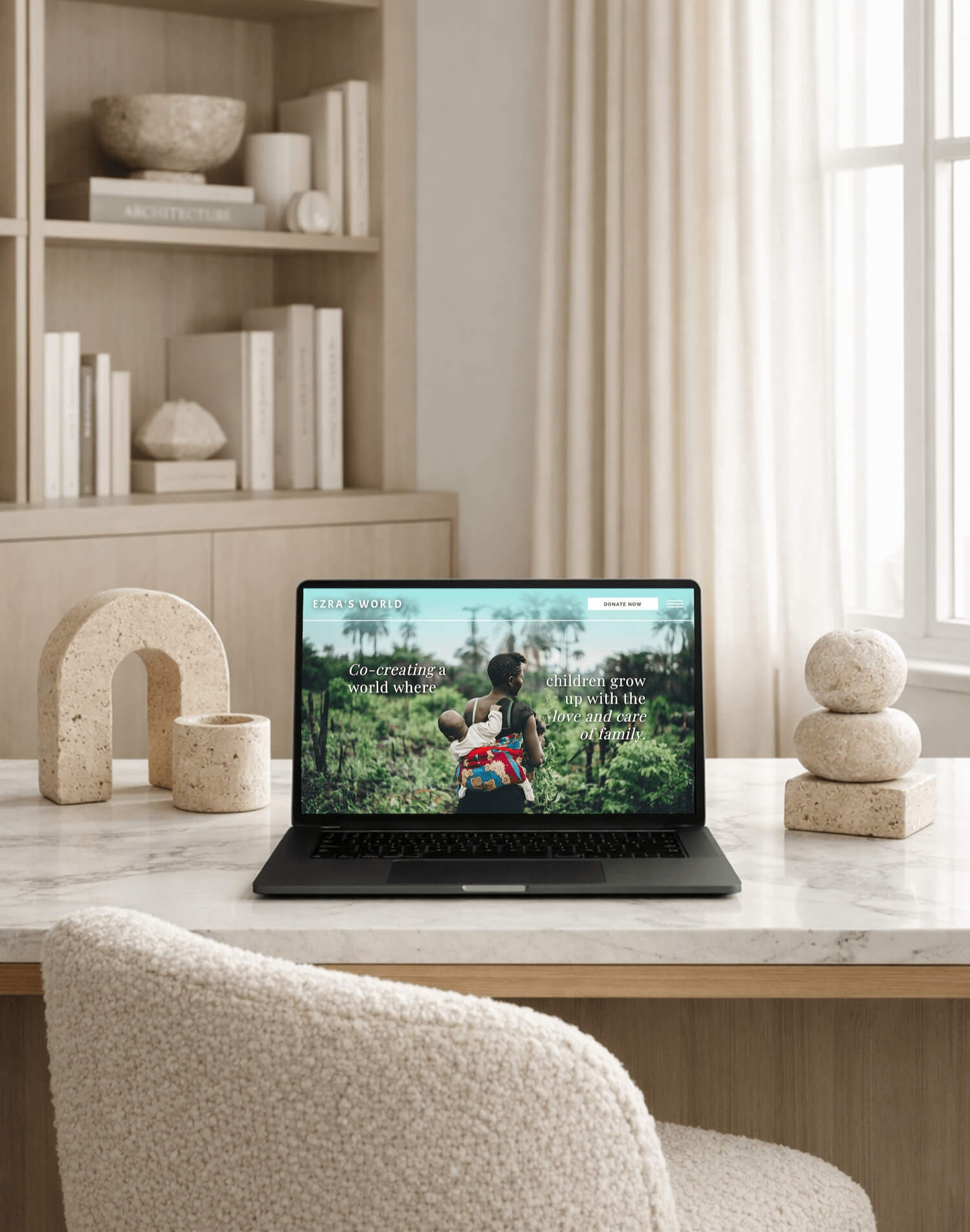 Laptop showing Ezra’s World nonprofit website on a desk with neutral decor and shelving